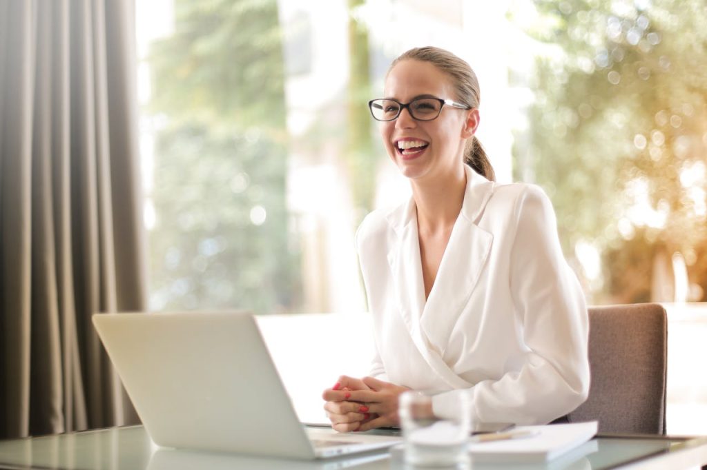 pexels-photo-3756679 Cheerful businesswoman in glasses working on a laptop, in a bright and modern office setting.